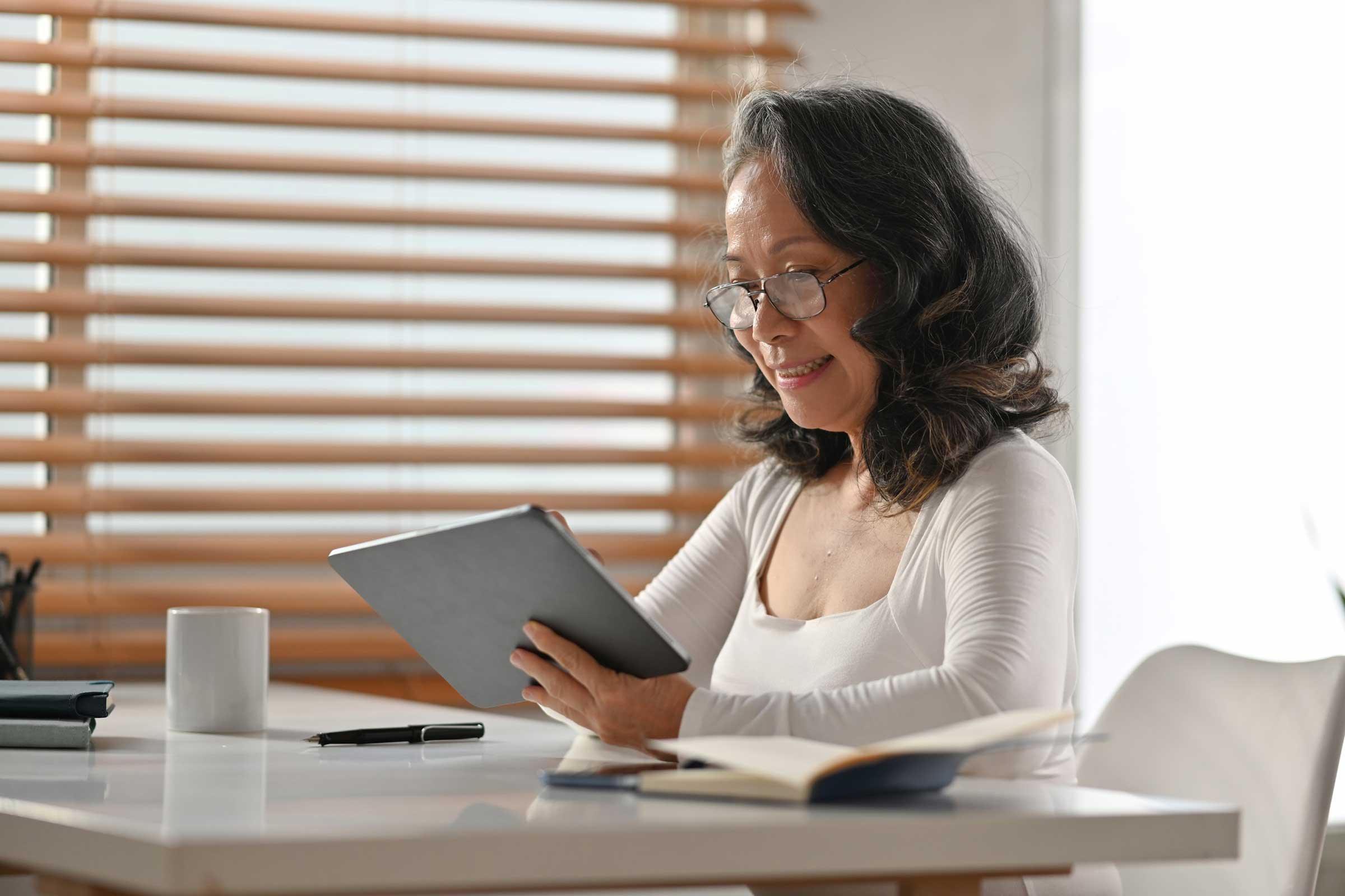 Woman sat at a table with glasses on and a table in her hands