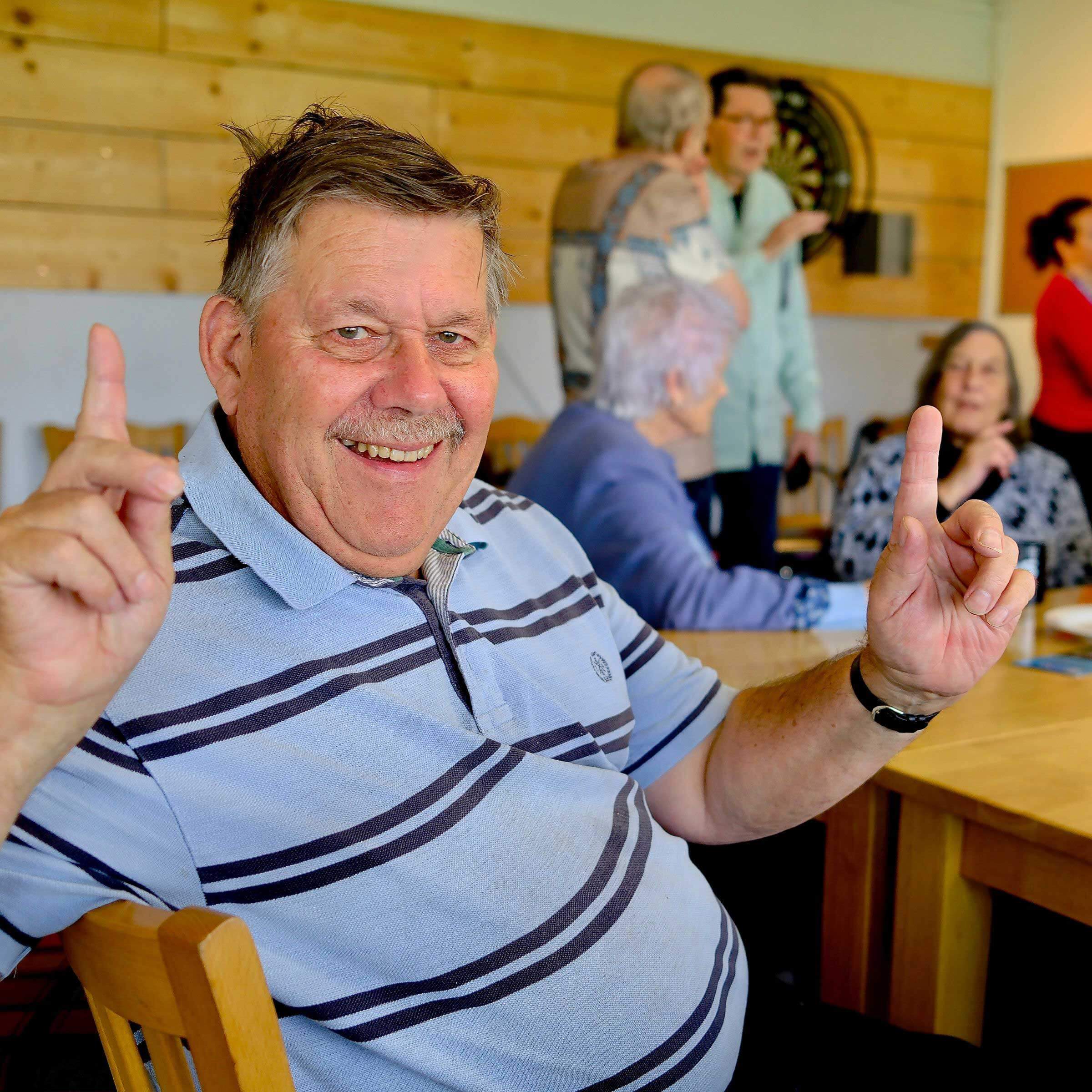 Man looking at the camera with both hands up with a single finger pointing up