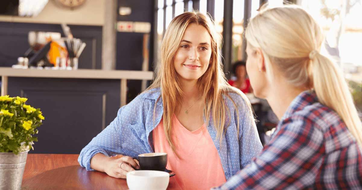 Woman looking at another woman both having a coffee sat at a table
