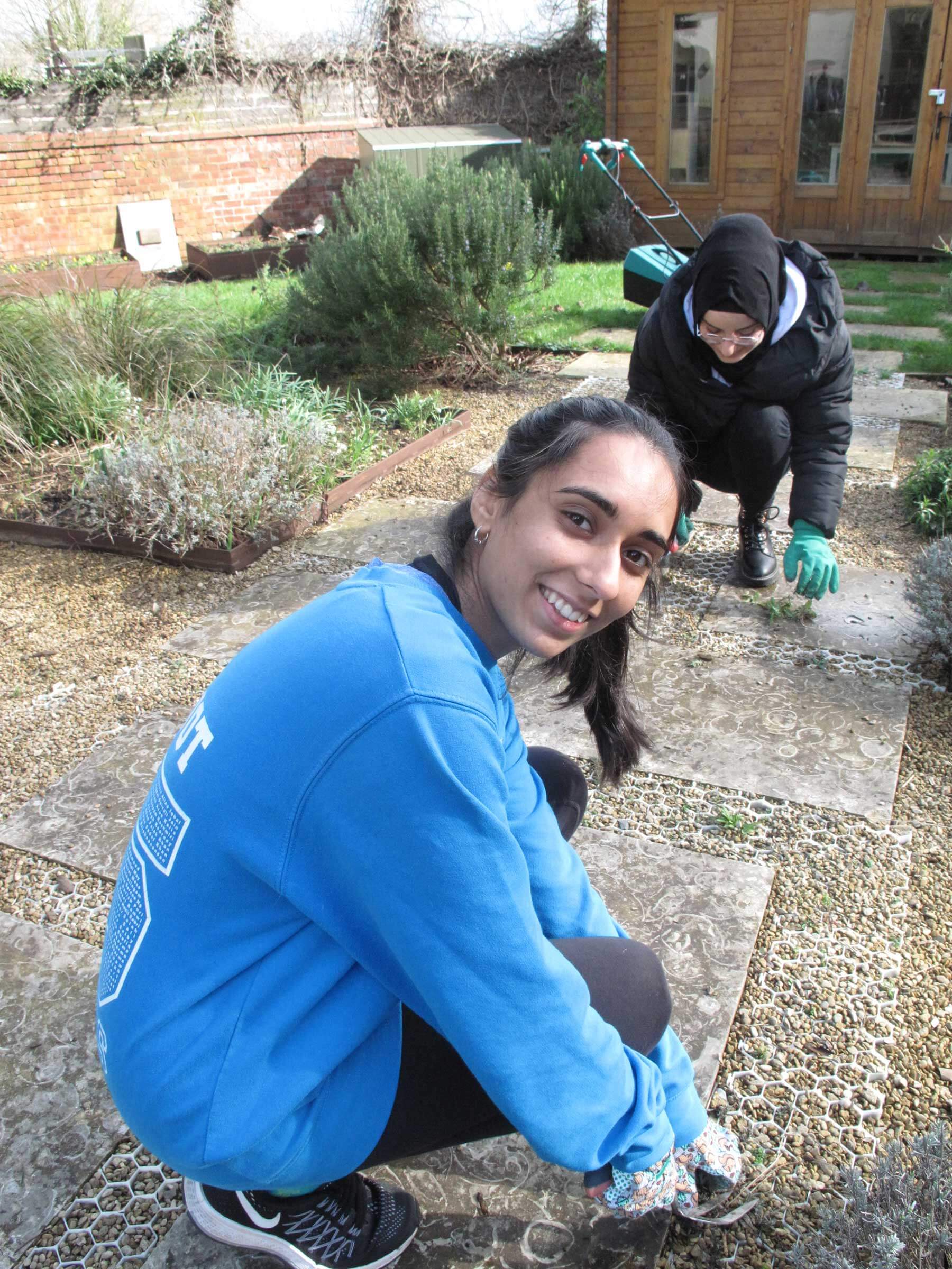 Two girls in the garden, gardening with one looking at the camera smiling