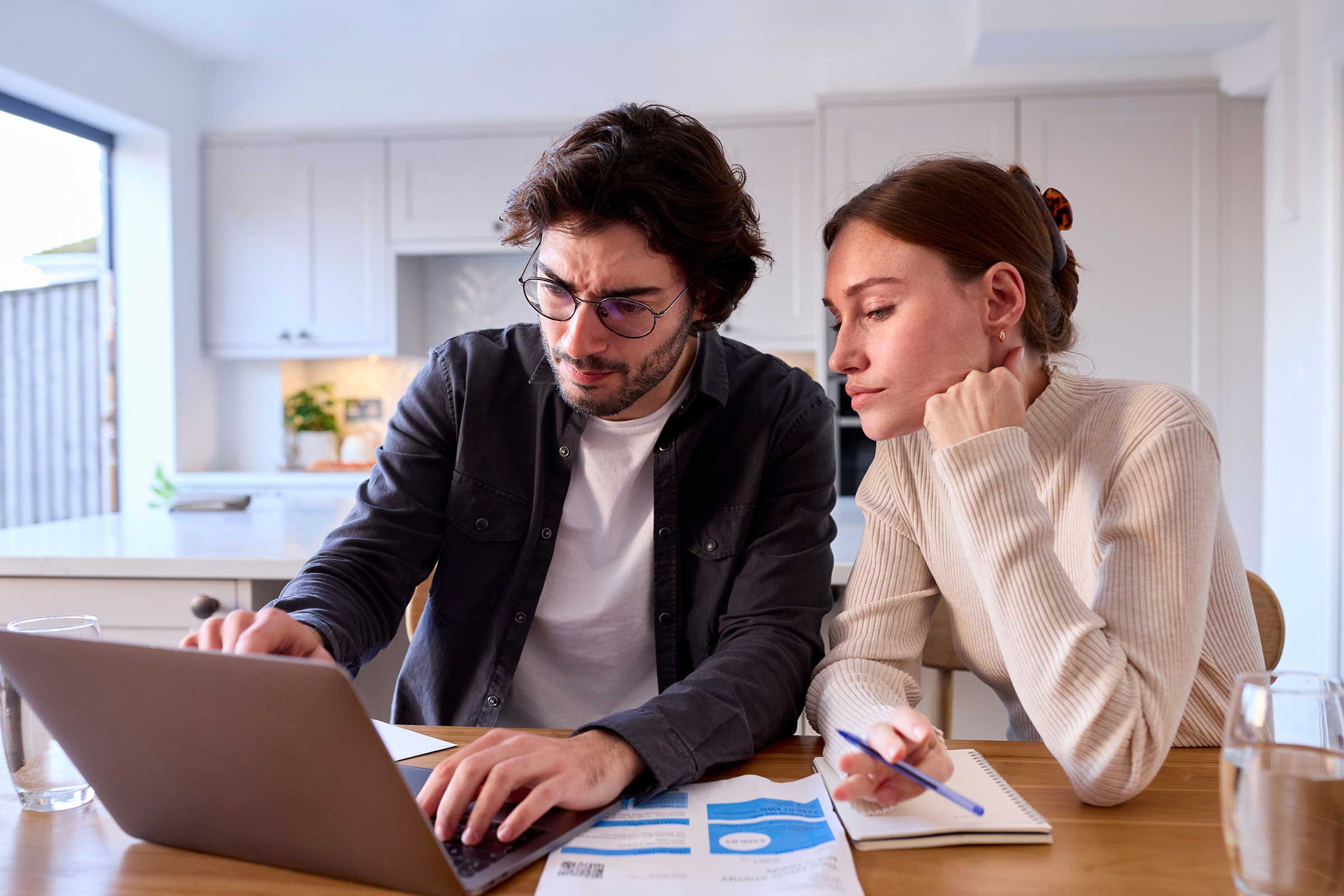 Couple sat at table in front of a laptop with an energy bill on the table 