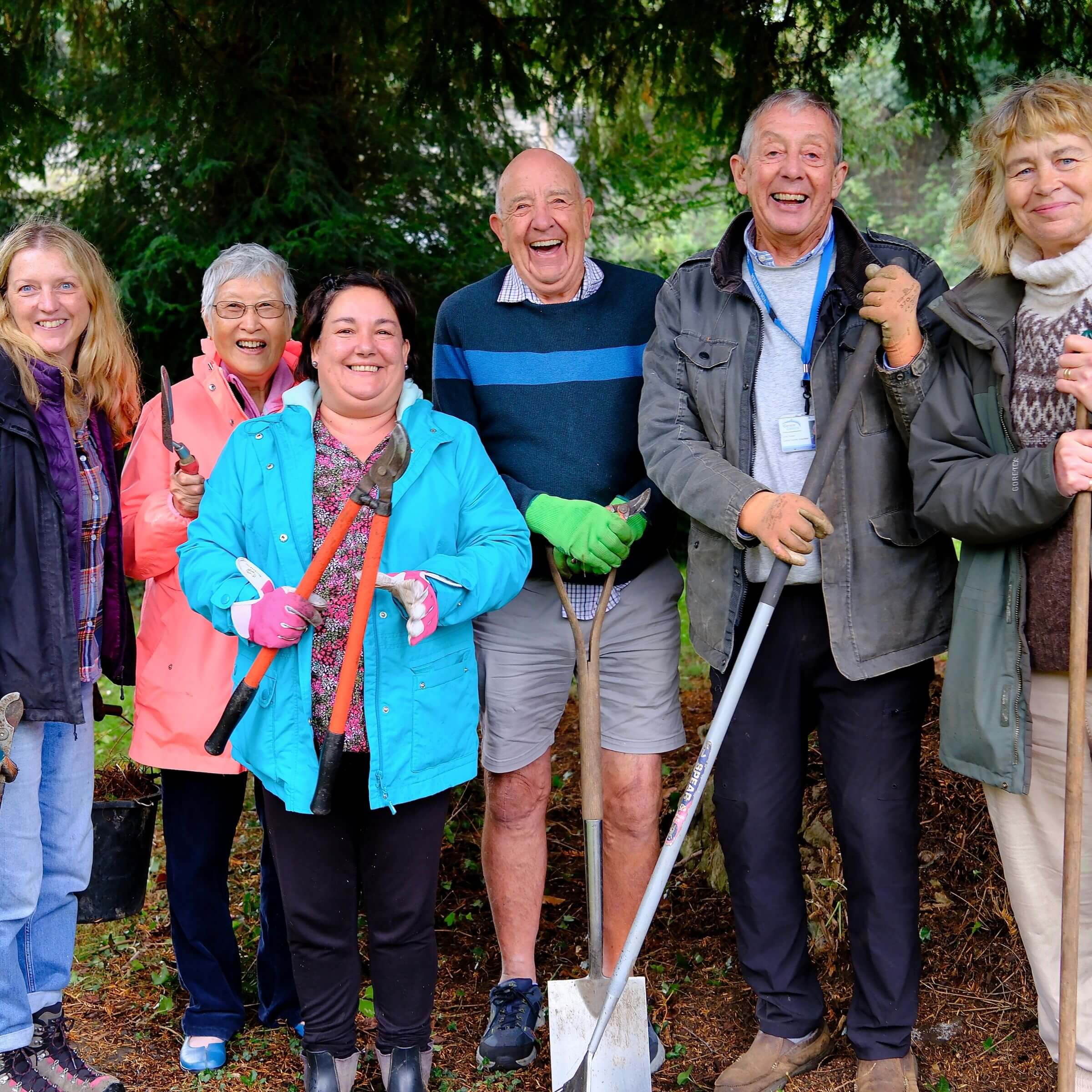 people stand together in a lush green garden holding gardening equipment