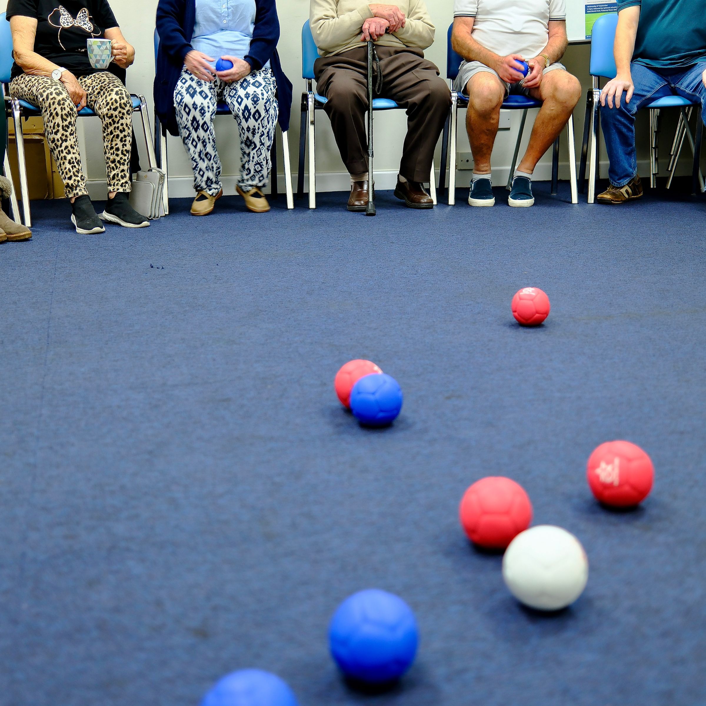 red, blue and white boccia balls and people sat on chairs in the background