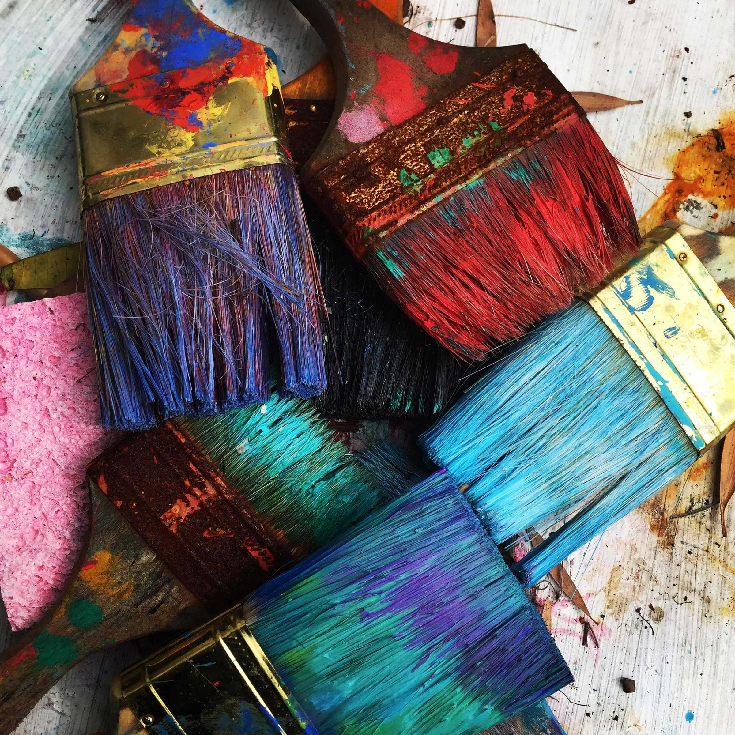 Pile of paint brushes with different colour paints on them