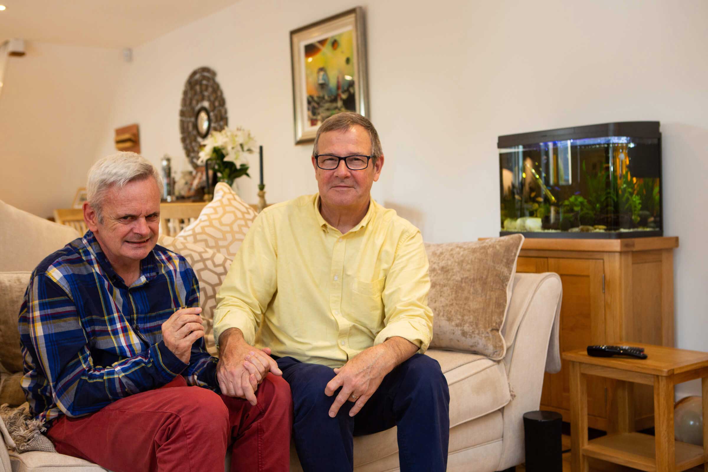 Mike adult carer with his partner Tom sat on a sofa holding hands