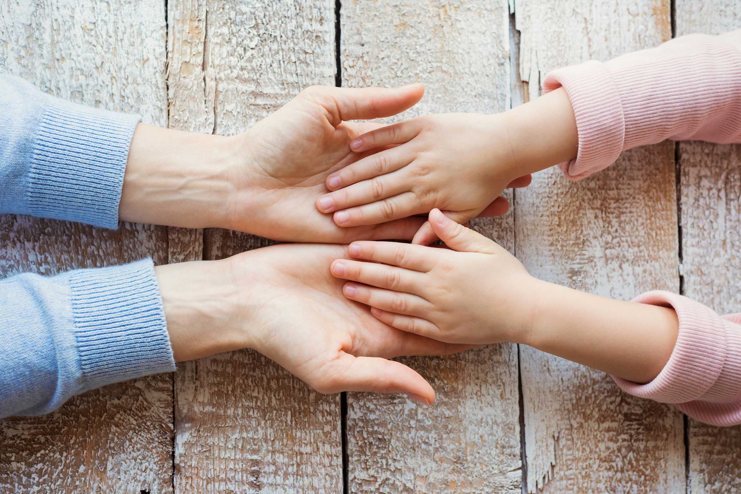 Adult hands laid out facing up with child hand placed in each palm