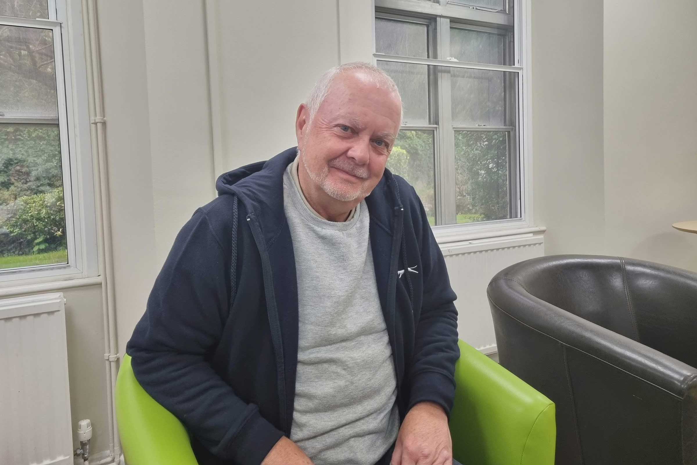 Man sat in a green chair smiling at the camera