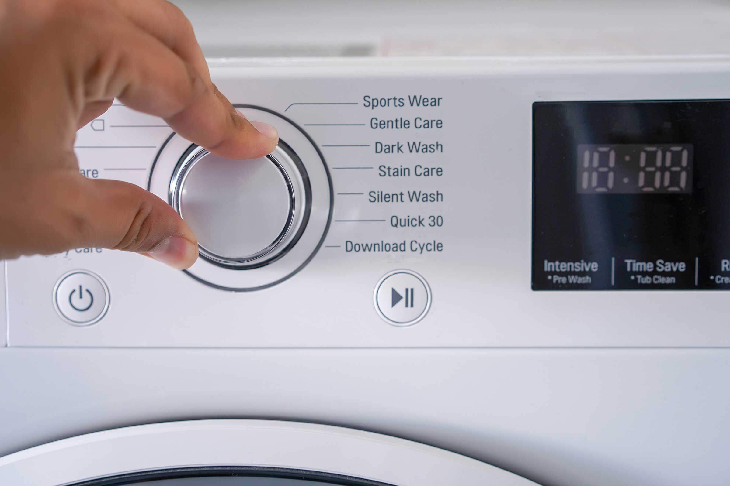 Close up of a washing machine and someone turning the dial