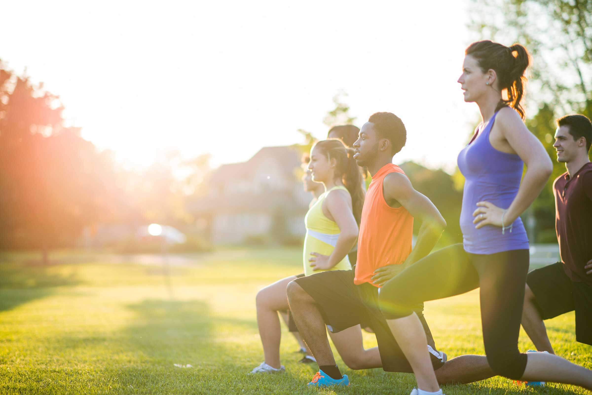 Group of adults doing lunges exercise outside on the grass