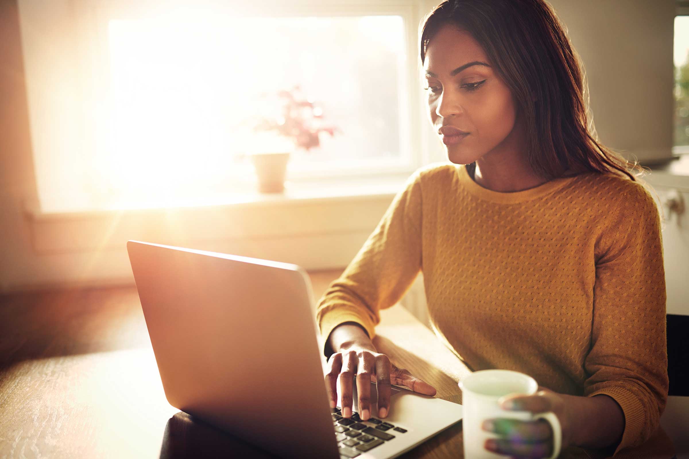 Woman on a laptop with a mug of coffee in her hand