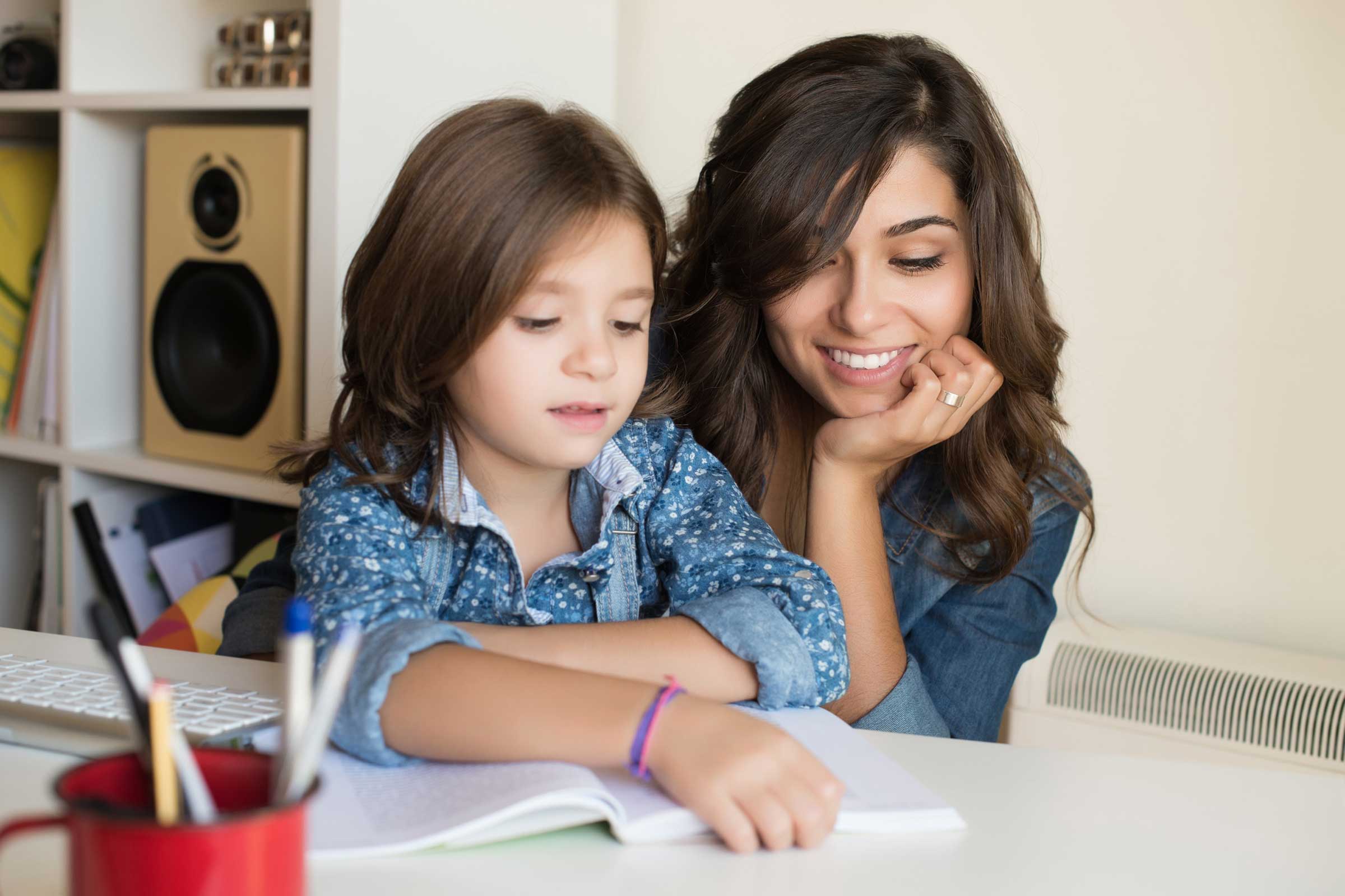 Child reading at a table with a women sat with her