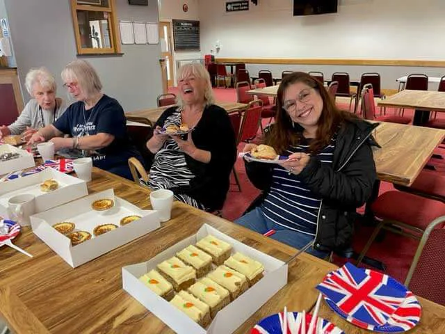Group of people sat around a table with cakes on with two women holding up their plates