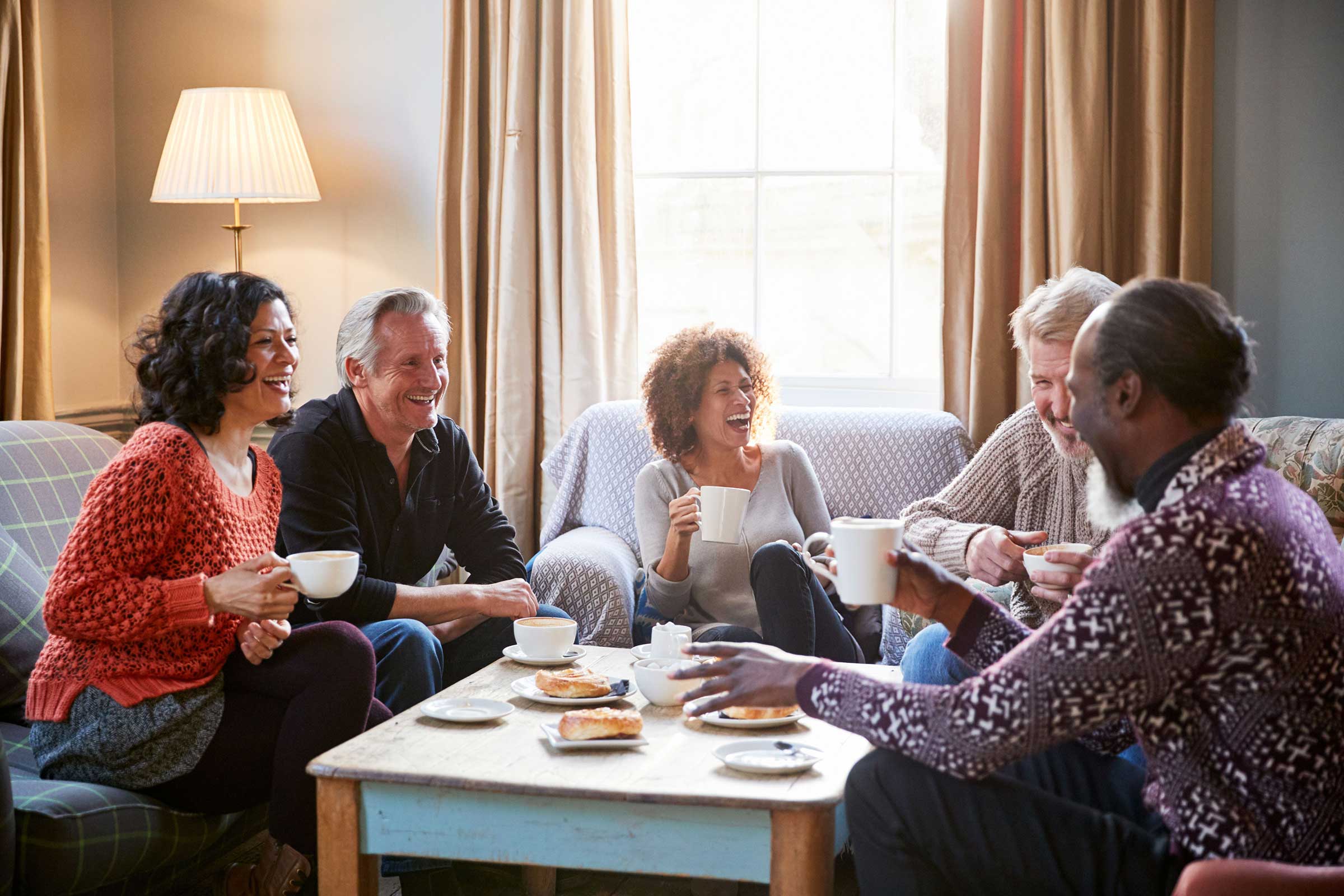 Group of people sat down eating cake and drinking tea chatting