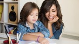 Image of a mum with long brown hair watching her child read a book