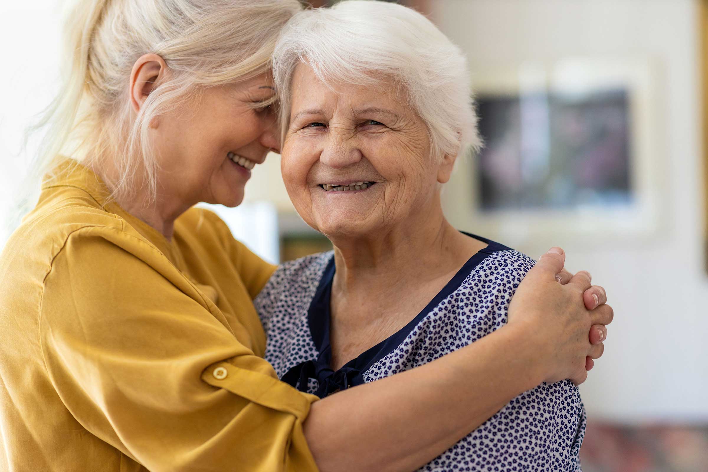 Old lady looking at the camera while a lady hugs her from the side