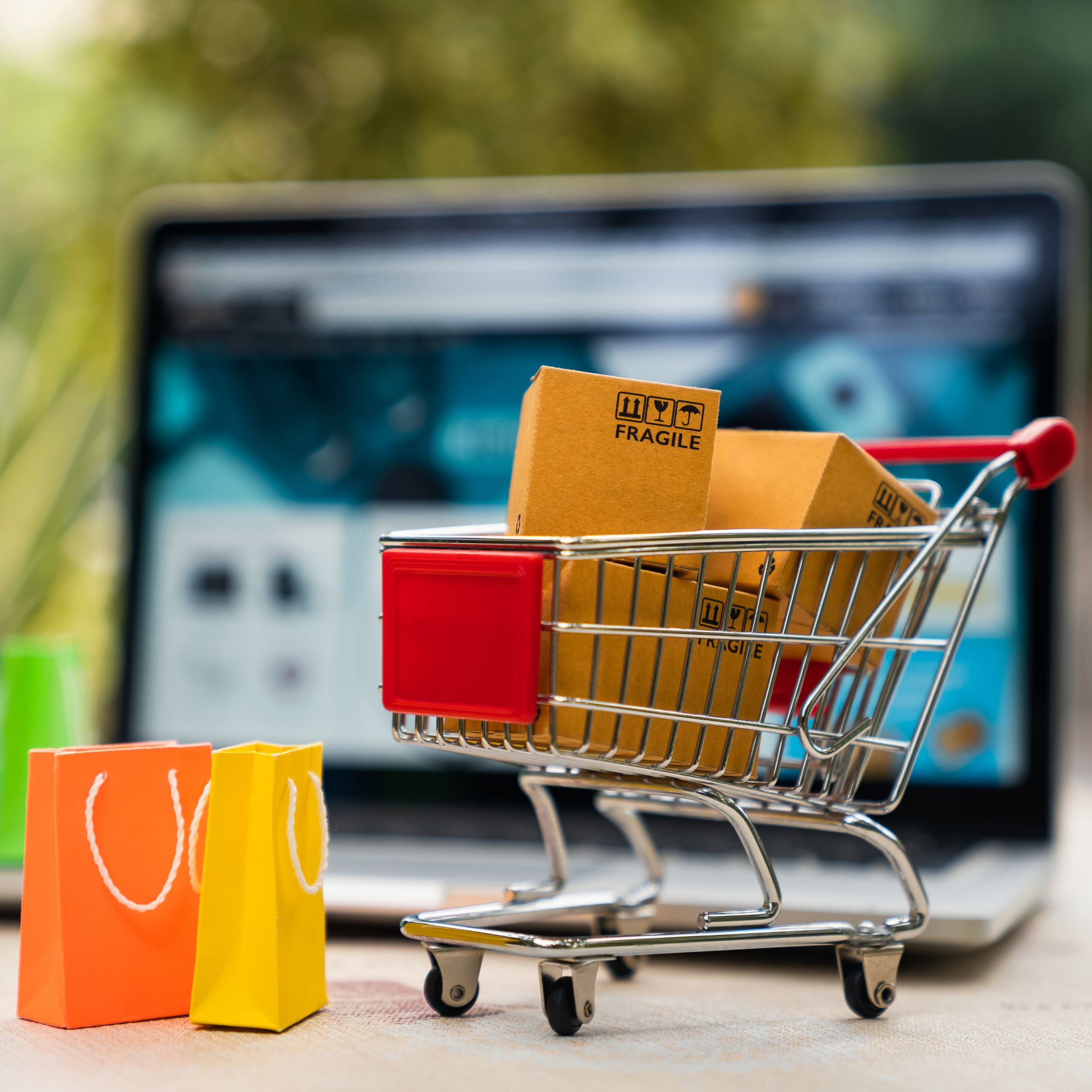 Photo of a shopping cart in front of a laptop and shopping bags alongside