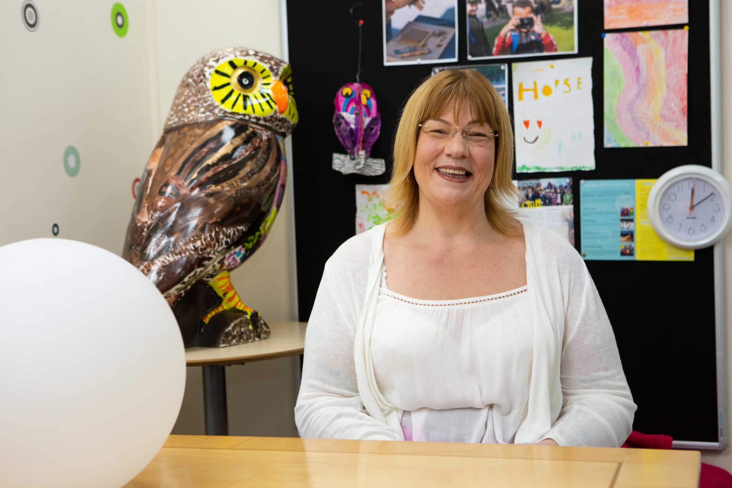 Woman smiling at the camera with childrens craft pictures behind her