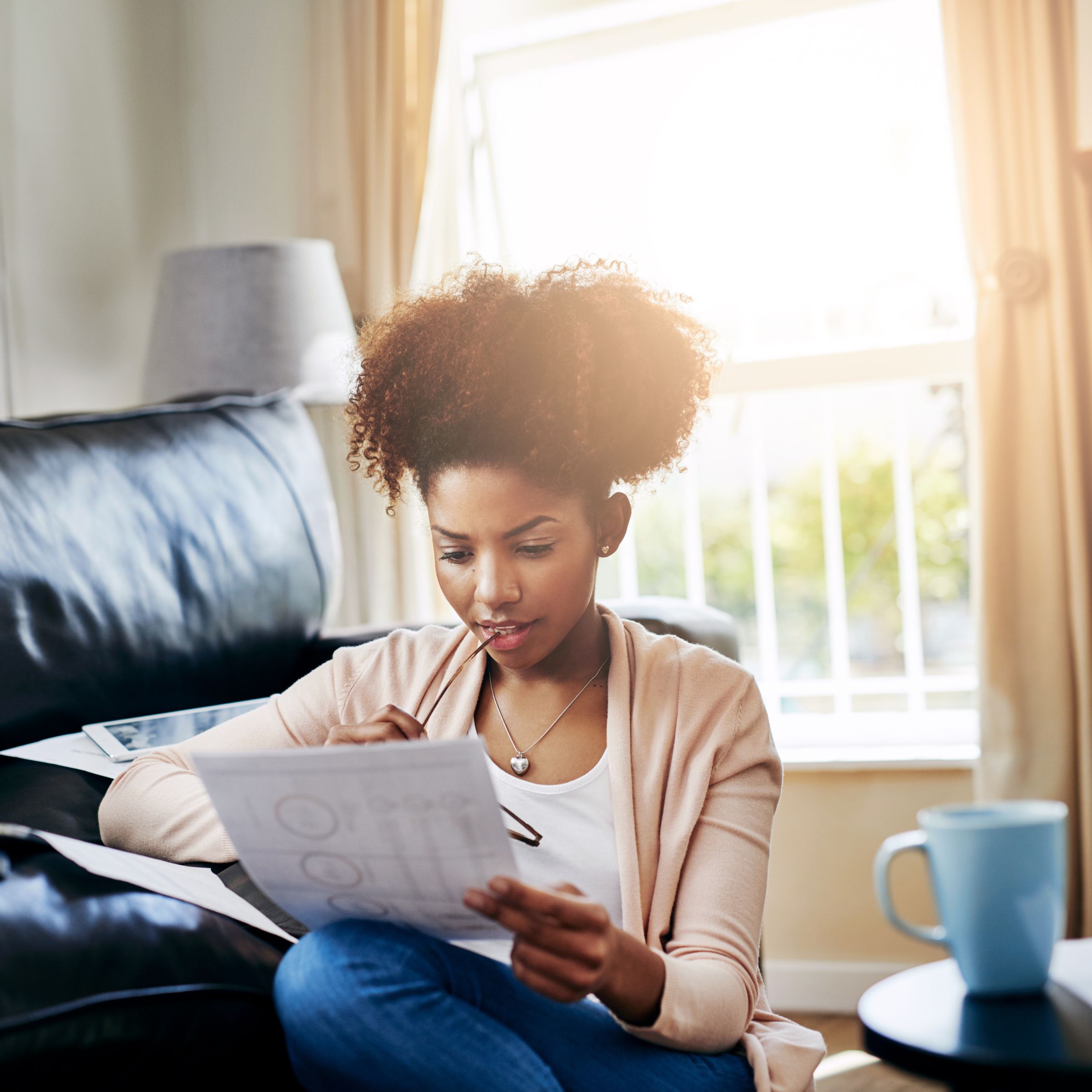 women looks down at a document holding her glasses with a cup of tea nearby
