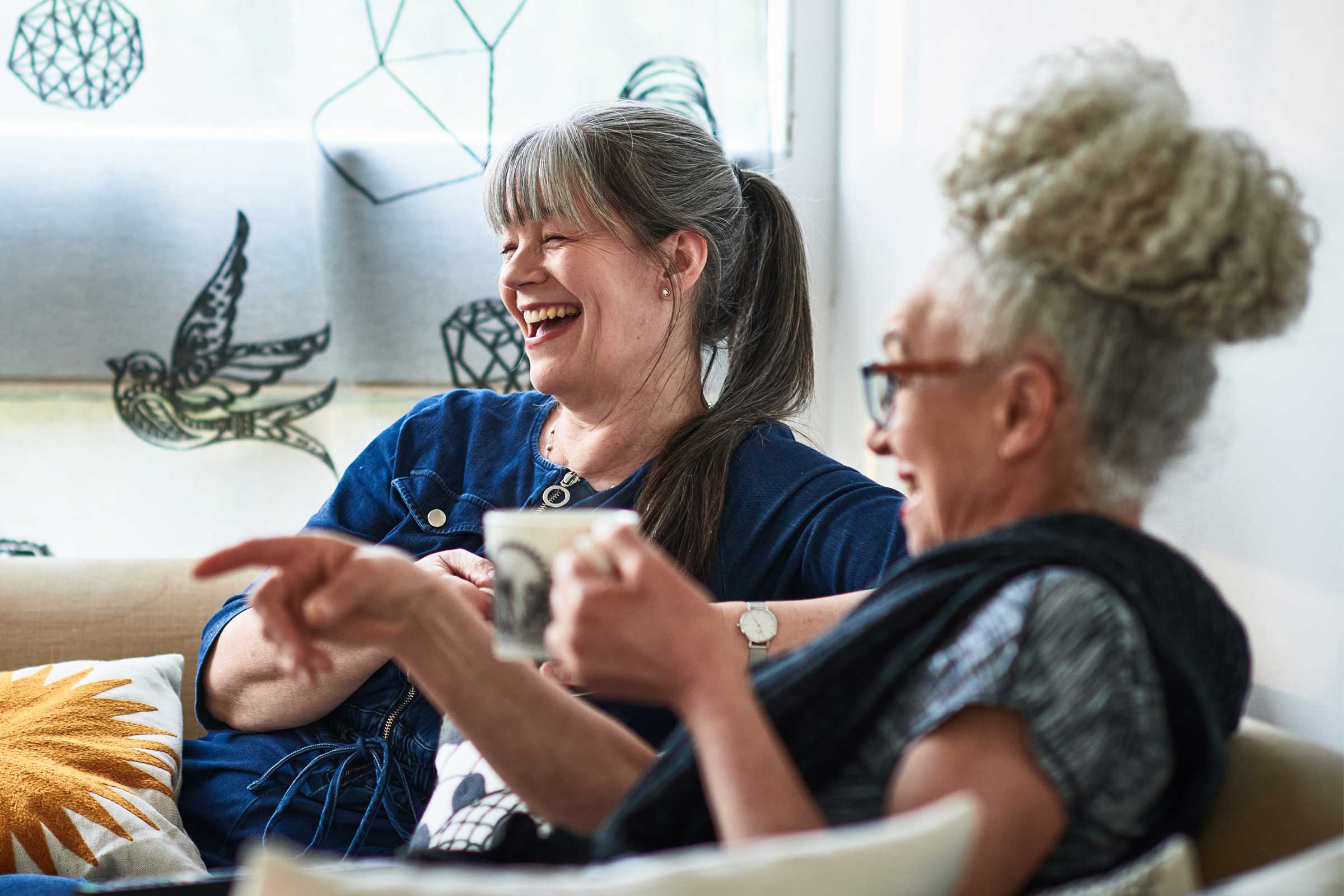 Two women sat having a coffee laughing at something off camera