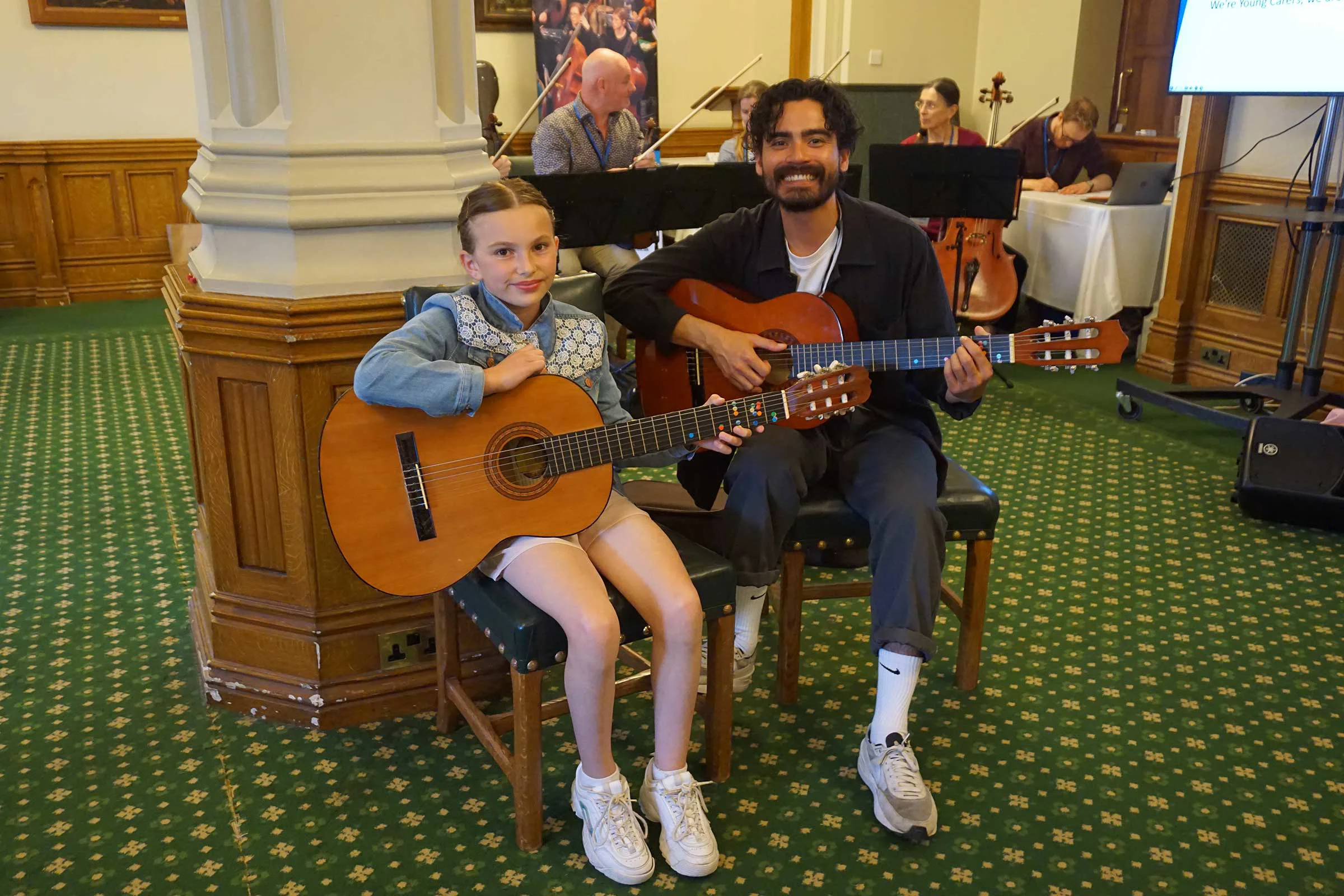Young carer and Mike with guitars on their laps smiling at the camera
