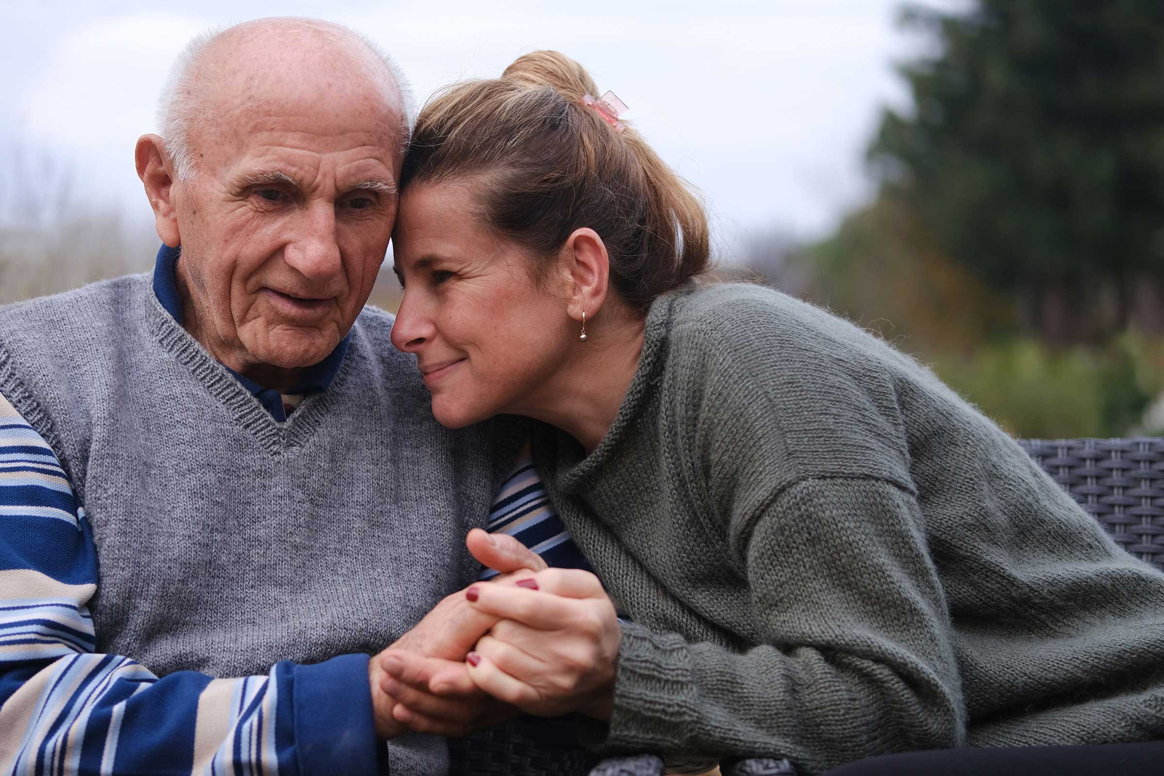 Old man with a woman holding his hands resting her head on his